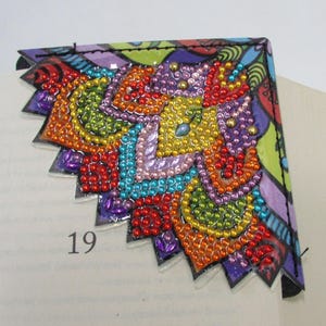 May include: A colorful, handmade corner bookmark with a beaded design. The bookmark features a vibrant array of colors including red, orange, yellow, green, blue, purple, and pink. The number 19 is visible on the page.