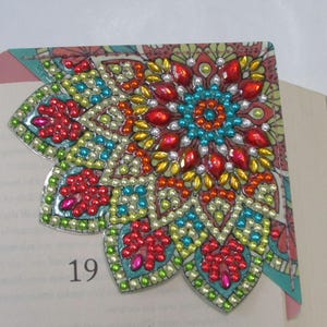 May include: A decorative corner bookmark with a colorful, jeweled mandala design. The bookmark features red, orange, blue, and green gems and beads. The number 19 is visible on the page.