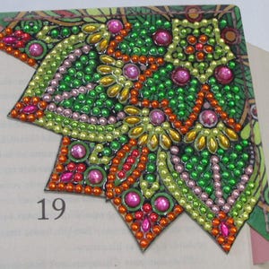 May include: A decorative corner bookmark with a colorful, jewel-like design. The bookmark features a pattern of green, orange, pink, and yellow embellishments. The number 19 is visible on the page. A unique accessory for book lovers.