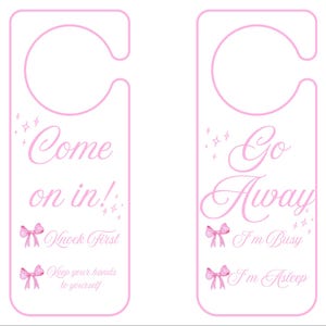 Pode incluir: Dois cabides de porta cor-de-rosa com um recorte para a maçaneta. Um diz "Come on in!" com "Knock First" e "Keep your hands to yourself" abaixo. O outro diz "Go Away" com "I'm Busy" e "I'm Asleep".