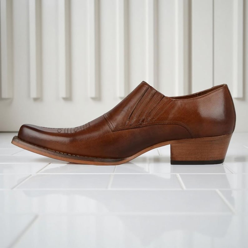 May include: A brown leather cowboy boot with a square toe and a stacked heel. The boot has a low-cut design and a decorative stitch pattern on the vamp. The heel measures approximately 2 inches.