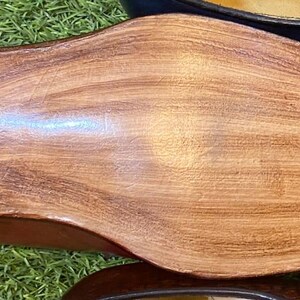 May include: Close-up of the sole of a brown leather shoe with a dark gray heel. The shoe's sole has a wood-grain texture. Other leather shoes in blue and black are visible in the background.