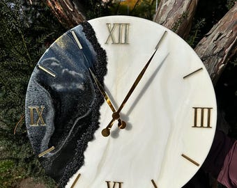 Peut inclure: Horloge murale ronde avec un motif marbré blanc et noir. L'horloge présente des chiffres romains et des aiguilles dorées. L'horloge est accrochée à une branche d'arbre.