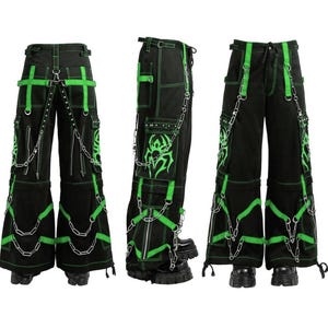 May include: Black cargo pants with neon green accents, stitching, and straps. The pants feature multiple pockets, decorative chains, and a tribal design on the pockets. The pants have a wide leg design.