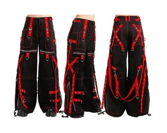 May include: Black cargo pants with red accents, featuring multiple pockets, zippers, and straps. The pants have a wide leg design and are displayed from multiple angles, showcasing the details of the construction and the bold color contrast.