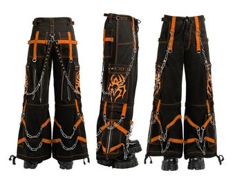 Puede incluir: Pantalones negros con detalles naranjas, cadenas y costuras decorativas. Los pantalones cuentan con múltiples bolsillos, correas y un diseño único. Los pantalones se muestran desde múltiples ángulos.