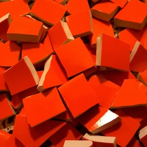 Puede incluir: Un montón de azulejos de mosaico de cerámica de color naranja brillante. Los azulejos son de varias formas y tamaños, algunos son cuadrados y otros triangulares.
