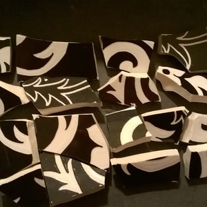 May include: A collection of black and white ceramic tile pieces with a floral pattern. The tiles are broken into various shapes and sizes.