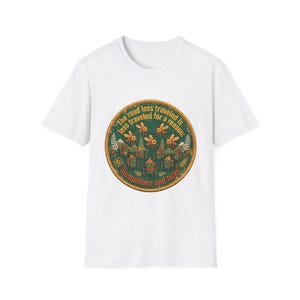 May include: A white short-sleeve t-shirt featuring a circular graphic with a green background. The text reads, "The road less traveled is less traveled for a reason: mosquitoes and ticks." The design includes illustrations of insects and hikers.