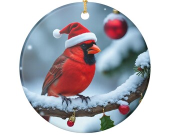 Könnte beinhalten: Runder Weihnachtsschmuck mit einem leuchtend roten Kardinalvogel mit Weihnachtsmütze, der auf einem schneebedeckten Ast sitzt. Der Schmuck hat eine goldene Schnur zum Aufhängen und ist mit roten Kugeln und Stechpalmen verziert.