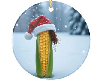 Puede incluir: Adorno navideño redondo con una mazorca de maíz con un gorro de Papá Noel. El maíz es amarillo, con hojas verdes y sedas marrones. El gorro es rojo con ribete blanco y pompón. El fondo es una escena invernal nevada.