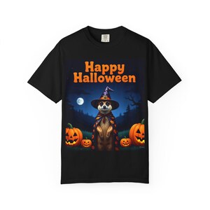 May include: Black t-shirt featuring a Halloween design. The graphic shows a meerkat wearing a witch hat and cape, surrounded by jack-o'-lanterns and the text "Happy Halloween". A full moon and trees are in the background.