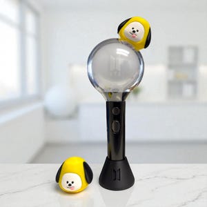 Op de afbeelding: Een zwarte en zilveren lichtstaaf met een heldere bol en de tekst "BTS". Een gele cartoon hond figuur zit bovenop de bol. Een bijpassende hond figuur zit onder de lichtstaaf. De lichtstaaf heeft een zwarte basis.