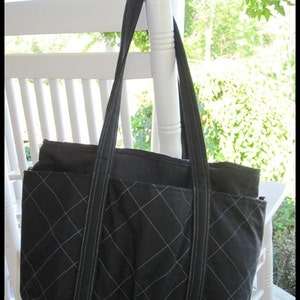 May include: A black quilted tote bag with two long straps. The bag has a diamond pattern and is hanging on a white chair.