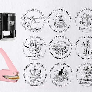 May include: A black self-inking stamp and a pink embosser are shown with several circular designs. Each design features the text "From the Library of Alexander Green" with various illustrations, including flowers, books, and a cat.