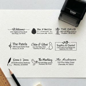 May include: A white sheet of paper featuring nine distinct black ink address stamp impressions, each with unique names, addresses, and icons like a pinecone, lighthouse, cat, and quill. A black Trodat self-inking stamp and a pencil are visible.