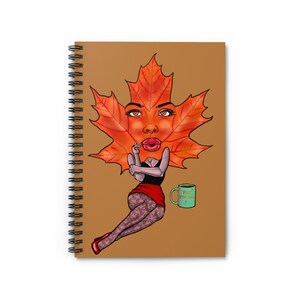 Può includere: Quaderno a spirale con copertina marrone. L'illustrazione mostra una foglia d'acero con un volto, che indossa un top nero e una gonna rossa. È visibile anche una tazza verde con la scritta "Fall For Me".