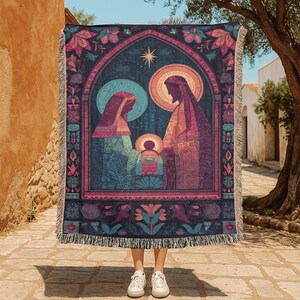 Könnte beinhalten: Eine gewebte Wandteppichdecke mit einer religiösen Szene im Stil eines Buntglasfensters. Die Decke hat einen dunkelblauen Hintergrund mit einem floralen Rand und Fransen. Das Kunstwerk zeigt eine heilige Familie mit einem Stern.