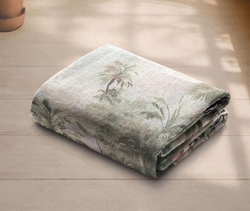 Pu&ograve; includere: Coperta rettangolare piegata con una stampa di foresta tropicale nei toni del verde, beige e marrone. La coperta presenta un design dettagliato di palme e altro fogliame. Il tessuto sembra essere un materiale tessuto.
