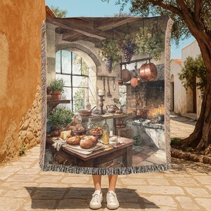 May include: A woven throw blanket featuring a watercolor painting of a rustic kitchen scene. The artwork depicts a stone fireplace, copper pots, and a table laden with food. The blanket has a fringed edge and is held up by a person wearing white sneakers.