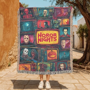May include: A colorful woven throw blanket featuring a collage of horror movie characters and scenes displayed on vintage television screens. The blanket has a fringed edge and the words "HORROR NIGHTS" are prominently displayed.