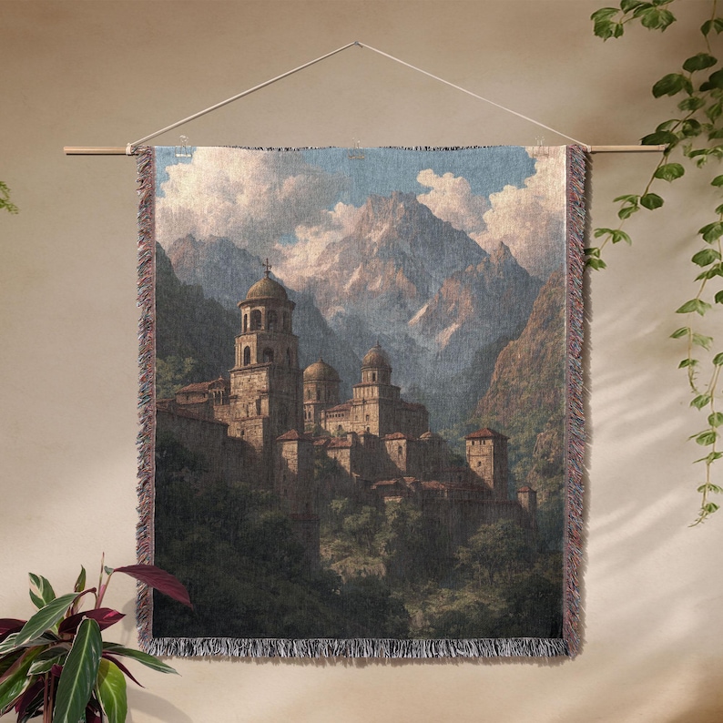 May include: Woven wall tapestry showing a mountain landscape with a medieval village. The tapestry features a detailed illustration of a stone village with domed towers and a cross on top. The colour palette includes shades of brown, green, and blue.