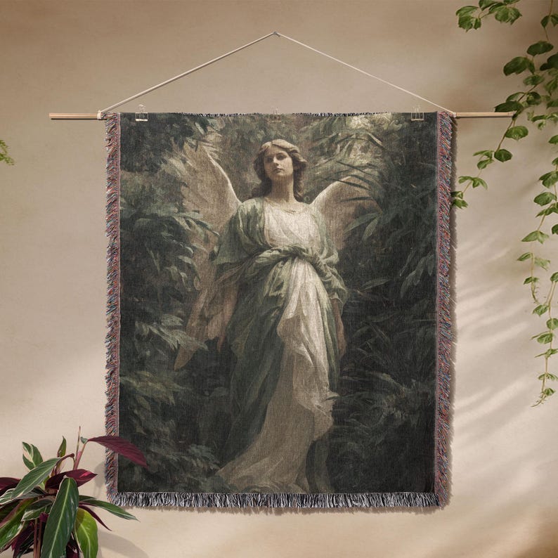 May include: A tapestry wall hanging featuring a classical painting of an angel with large wings, dressed in flowing robes, set against a backdrop of lush greenery. The artwork is framed with a fringed border and suspended from a wooden rod.