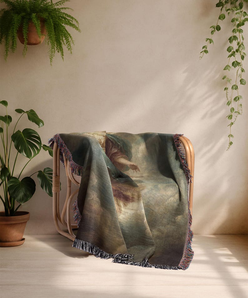 K&ouml;nnte beinhalten: Eine gewebte Decke mit einem Renaissance-Gem&auml;lde, drapiert &uuml;ber einem Korbstuhl. Die Decke hat eine Farbpalette aus Blau, Braun und Beige und gefranste Kanten. Die Szene spielt in einem Raum mit Pflanzen.