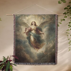 K&ouml;nnte beinhalten: Ein gewebtes Wandbehang mit einem klassischen Gem&auml;lde eines Engels mit ausgebreiteten Fl&uuml;geln vor einem bew&ouml;lkten Himmel. Der Engel tr&auml;gt flie&szlig;ende Gew&auml;nder in Rosa, Blau und Gold. Der Wandbehang wird an einer Holzstange aufgeh&auml;ngt.