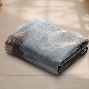 May include: Folded rectangular tapestry with a detailed architectural design, including a domed structure and a cloudy sky. The tapestry is mainly blue and brown, with visible folds and a textured appearance.