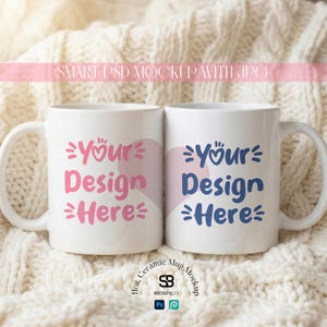 May include: Two white ceramic mugs with the text "Your Design Here" in pink and blue, with heart and star accents. The mugs are on a cream-colored knitted surface. The mugs are 11 oz.