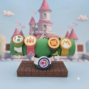 May include: Five silicone wristbands featuring Super Mario character designs, including a green Yoshi egg, a pink Princess Peach crown, a brown Donkey Kong DK logo with bananas, a yellow Mario M logo, and a white Toad mushroom cap icon.