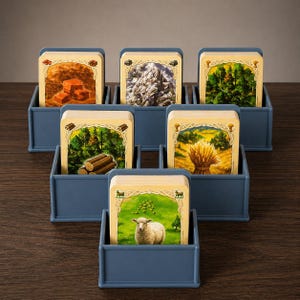 May include: A board game set with resource cards depicting various landscapes and resources, including forests, mountains, and fields. The cards are displayed in blue plastic holders, arranged on a wooden surface.