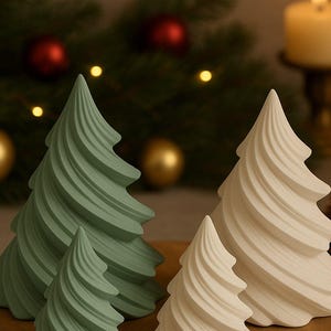 May include: Four decorative Christmas tree figurines in varying sizes. Two are a soft green, and two are off-white. The trees have a spiral design and are arranged on a wooden surface. A lit candle and Christmas ornaments are in the background.