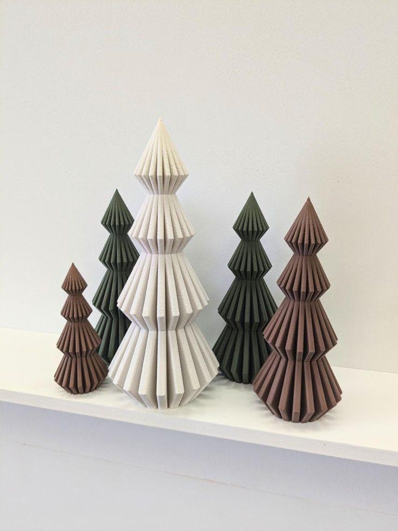 May include: A collection of decorative, geometric Christmas trees in varying sizes and colors. The trees are shades of brown, green, and off-white, with a textured, layered design. They are arranged on a white shelf against a white wall.