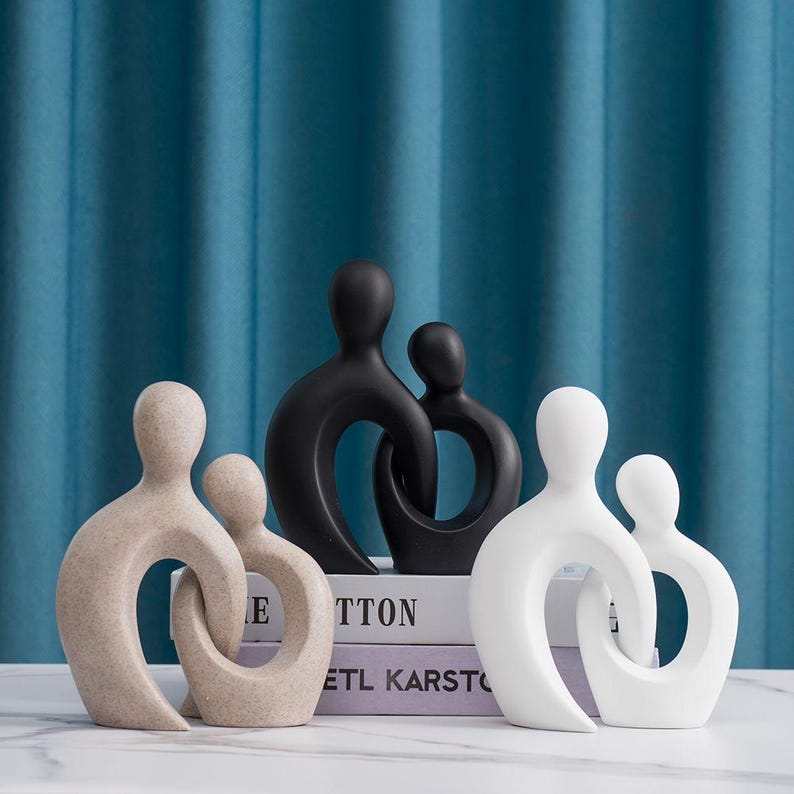 May include: A collection of abstract family sculptures in neutral tones. The sculptures are in black, white, and beige, with a minimalist design. The figures are intertwined, symbolizing unity and connection. The sculptures are displayed on a white surface.