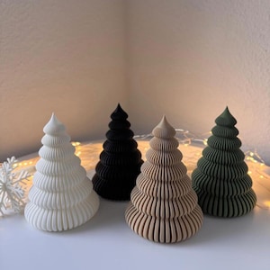 May include: Four decorative Christmas tree figurines in white, black, tan, and green. Each tree has a layered, ridged design. The trees are arranged on a white surface, with a snowflake and string lights in the background. The text "MACH3DRAUS" is in the upper right corner.
