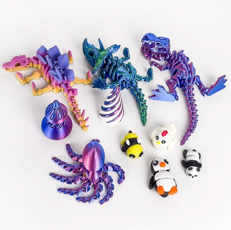 May include: A collection of colorful, articulated 3D-printed toys. The assortment includes dinosaur skeletons in shades of pink, purple, and blue, an octopus, and various animal figures like a penguin and panda.