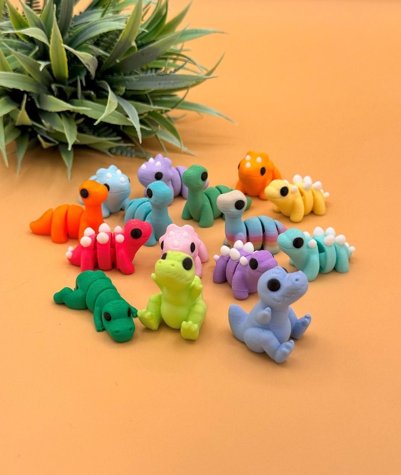May include: A collection of colorful, miniature dinosaur figurines in various poses. The dinosaurs are in shades of orange, red, pink, green, yellow, blue, and purple. Each dinosaur has a unique design, with some featuring segmented bodies and others with spiky details.
