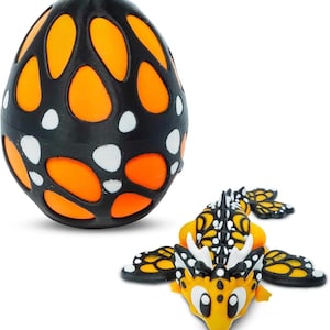 May include: A black and orange egg-shaped toy with a patterned design, next to a yellow and black dragon toy. The egg has orange cutouts and white dots. The dragon has wings and a detailed design.
