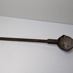 以下が含まれることがあります： 長い長方形の柄と丸みを帯びたボウルが付いた、濃い茶色の金属製おたま。 ボウルには片側に小さな注ぎ口があります。 おたまはヴィンテージまたはアンティークのようです。