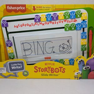 May include: A Fisher-Price StoryBots Slide Writer toy in its original packaging. The white writing board displays the word "BING" and has a sliding letter feature. The packaging is yellow and features cartoon characters and the text "Looks fun, Write?"