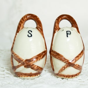 May include: A set of two ceramic salt and pepper shakers shaped like eggs with brown woven designs and the letters "S" and "P" on the front.