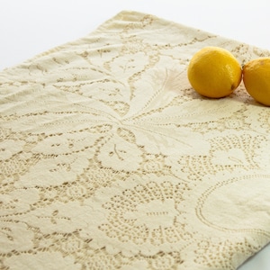 May include: A white crocheted tablecloth with a delicate floral pattern. Two yellow lemons are placed on the tablecloth.