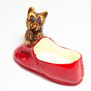 May include: A ceramic figurine of a brown and black Yorkshire Terrier dog sitting in a red slipper with the word "Mousehole" written on the side.
