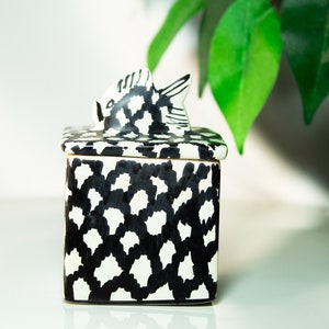 May include: A black and white ceramic box with a fish-shaped lid. The box has a geometric pattern and is perfect for storing small items.