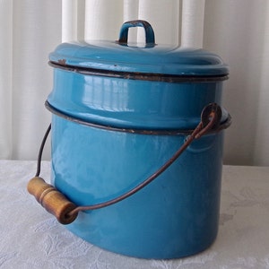 May include: A vintage teal blue enamelware double boiler with a wooden handle and a metal wire handle. The boiler has a lid with a metal handle.
