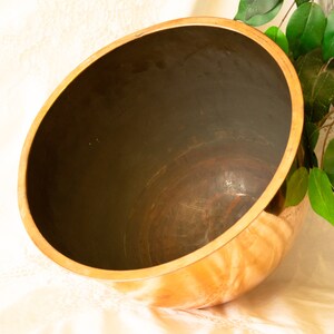 Puede incluir: Un cuenco grande, redondo, de cobre con un exterior brillante y pulido. El cuenco está vacío y tiene un interior marrón oscuro.