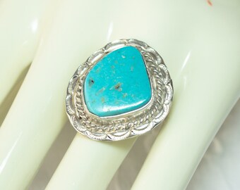 May include: A silver ring with a turquoise stone set in a detailed silver bezel. The stone is a light blue color with dark brown inclusions.