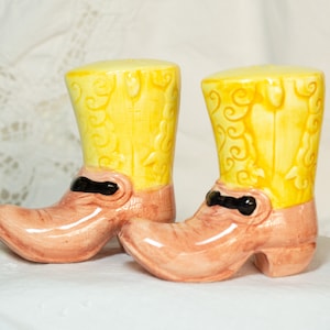 May include: A pair of ceramic cowboy boot salt and pepper shakers. The boots are yellow with brown trim and black accents.